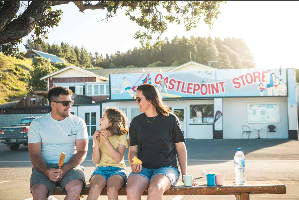 Family eating fish and chips in front of store along coast
