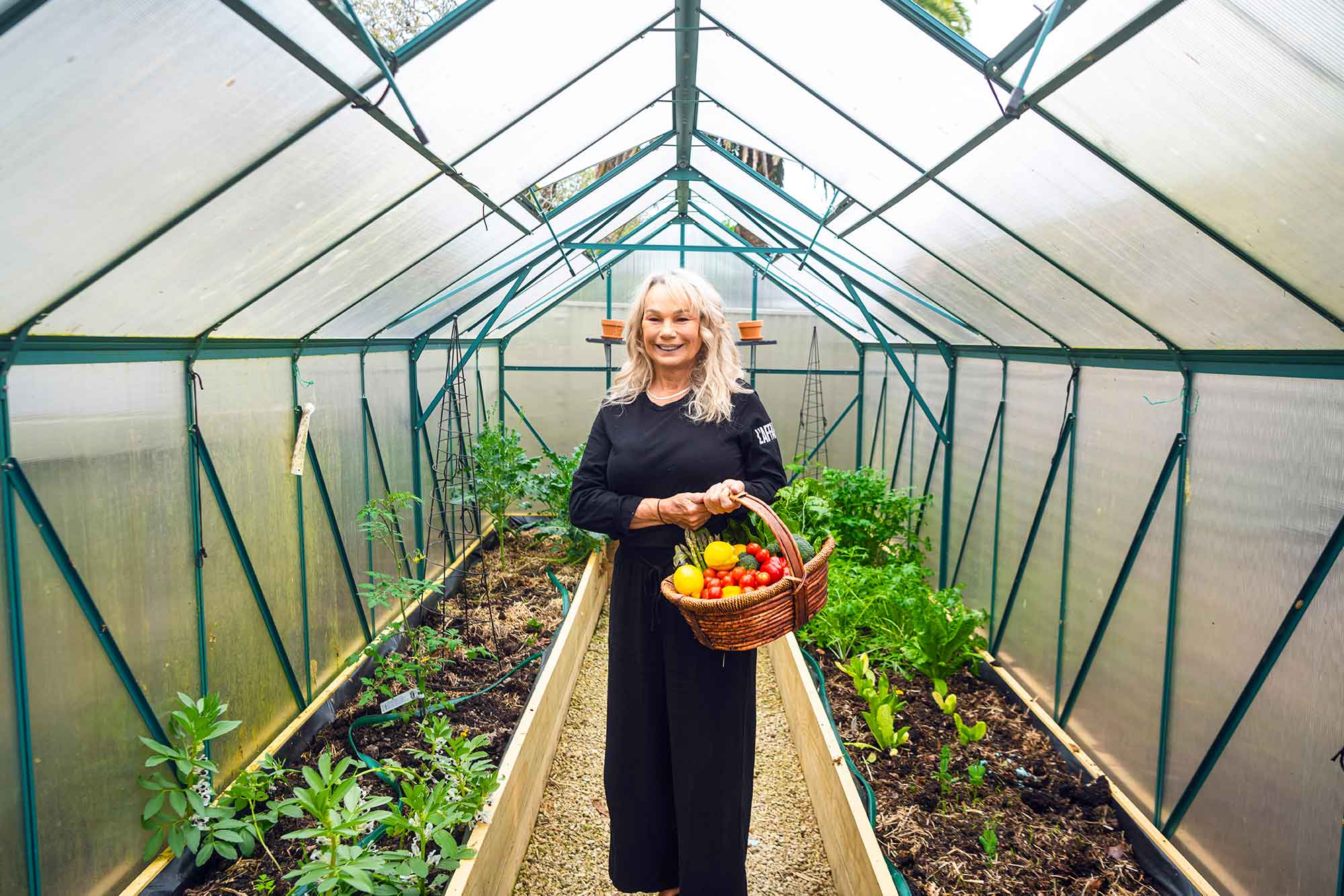 Woman standing in a greenhouse holding a basket of fresh vegetables.