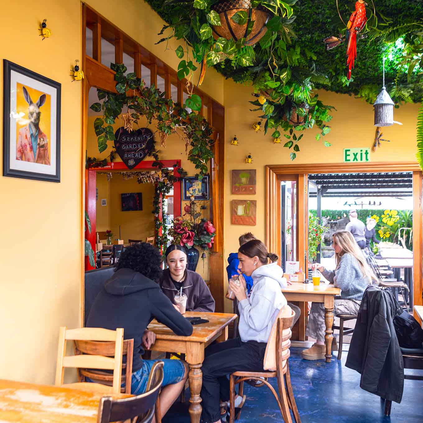 People sitting at tables in a cafe with yellow walls and greenery.