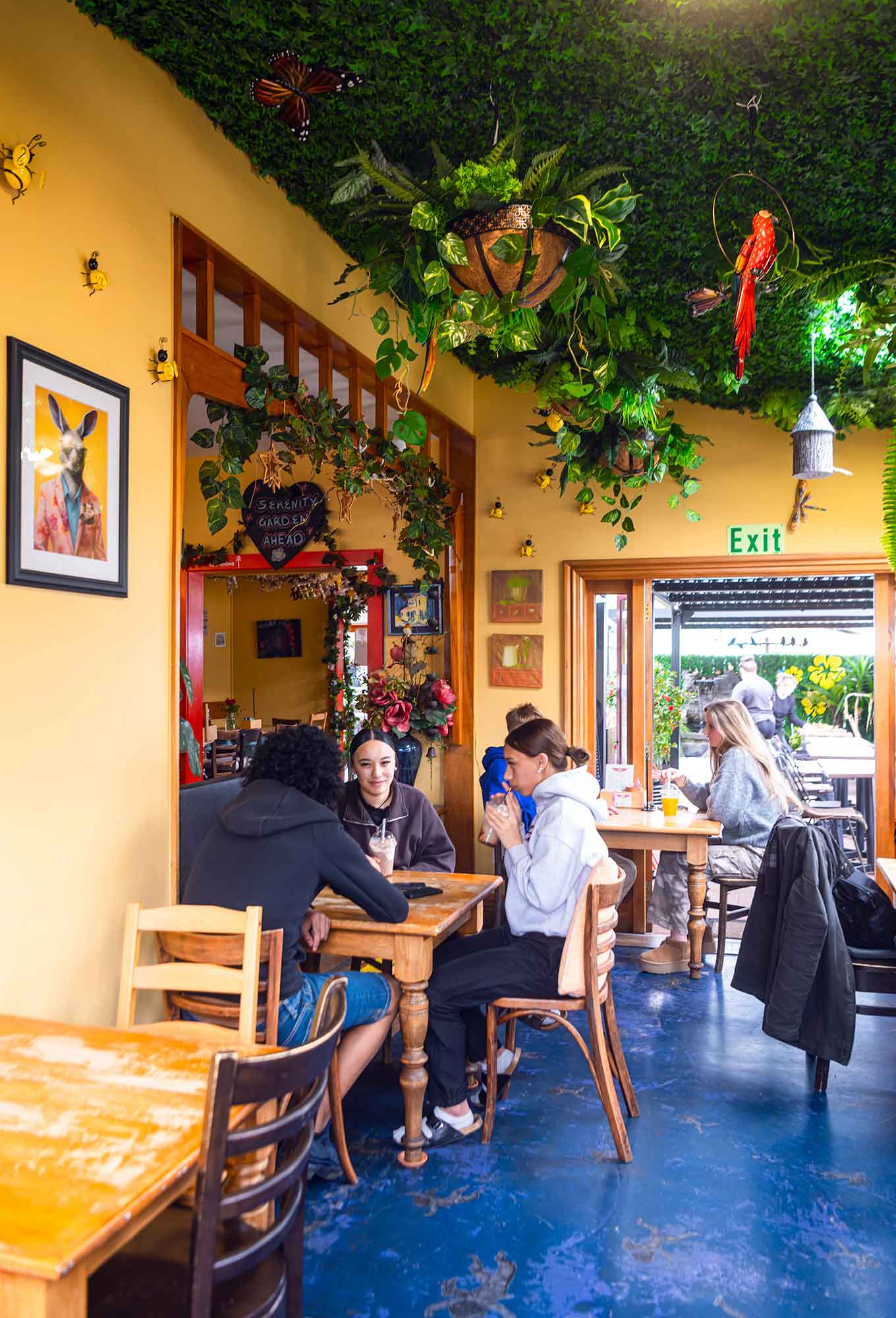 People sitting at tables in a cafe with yellow walls and greenery.