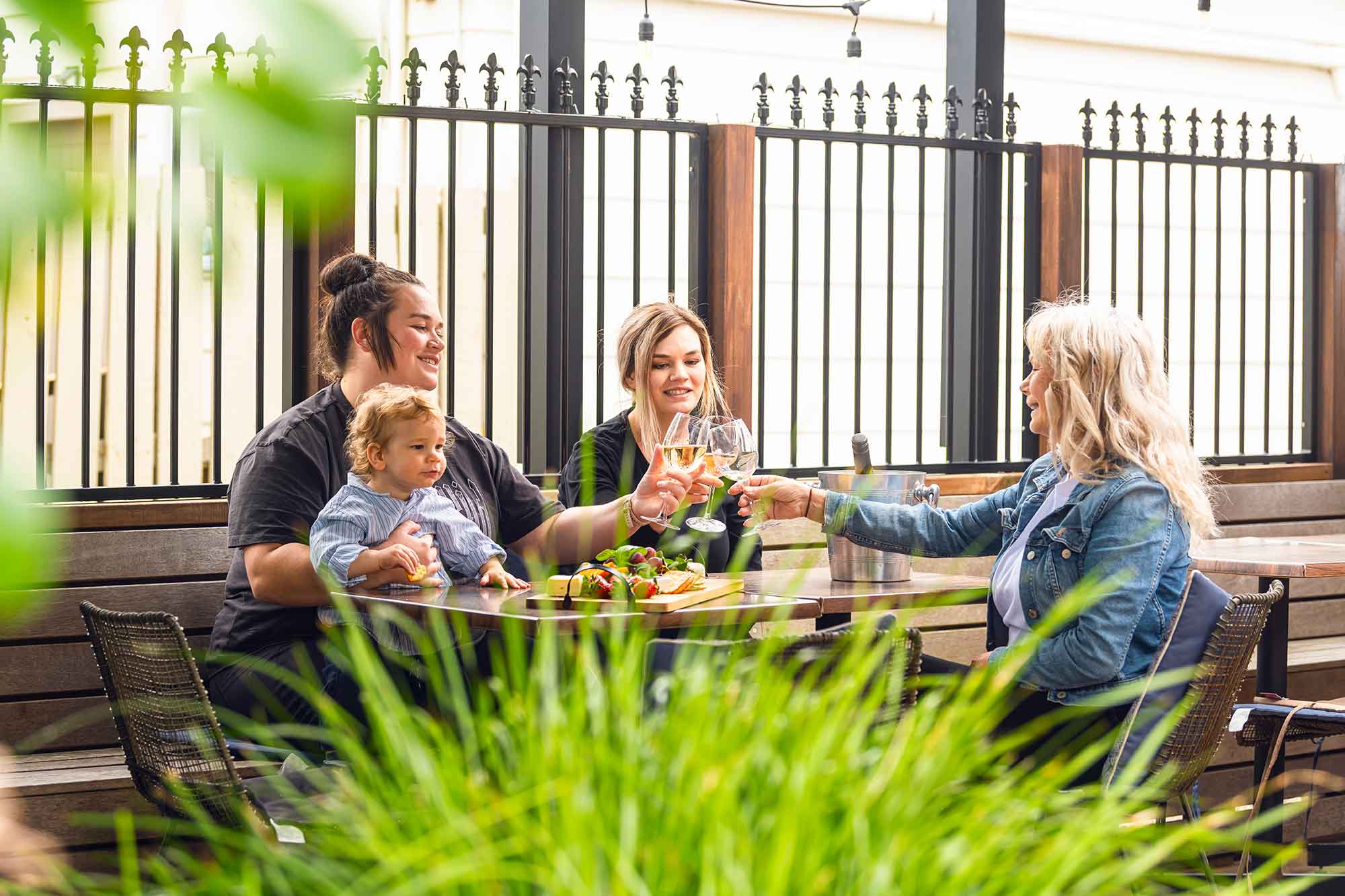 Three people sitting at an outdoor table with a child, enjoying a meal and drinks.