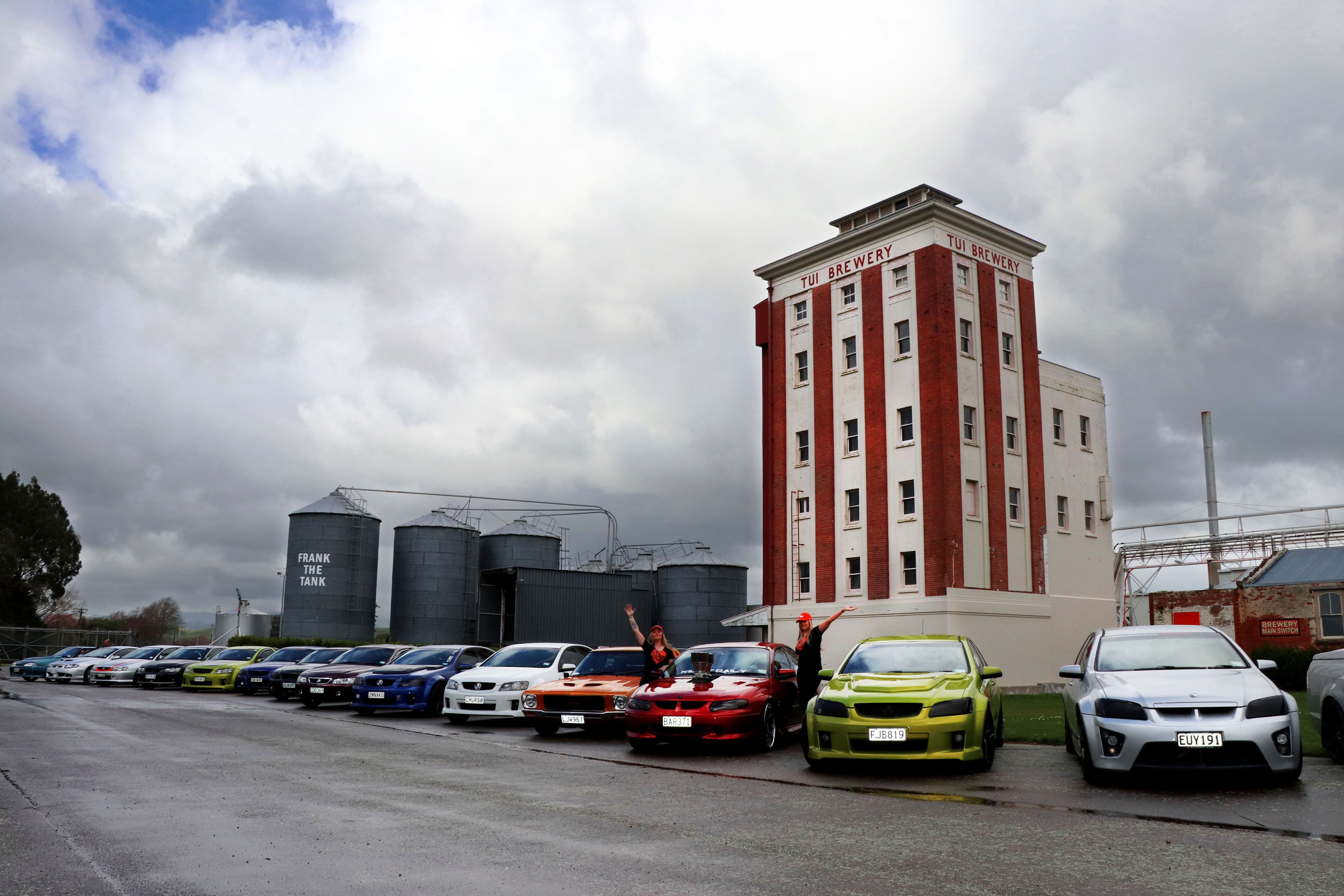 Girls beside classic cars in front of brewery tower 